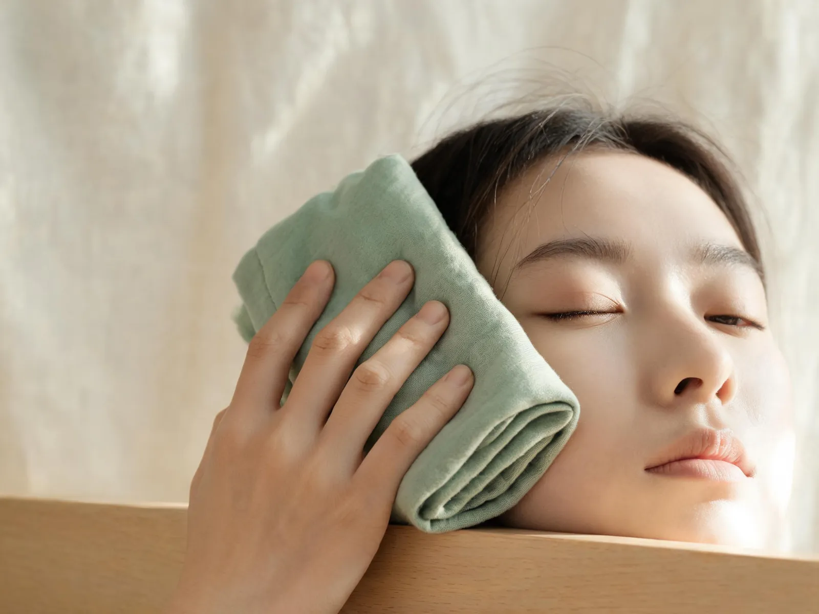 A hand pressing a folded cotton cloth against a cheek.
